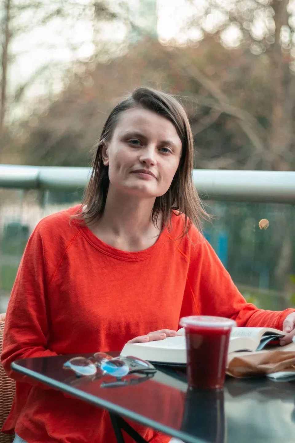 Georgia Blidar sentada en una terraza con un libro abierto y un jugo, mirando a la cámara