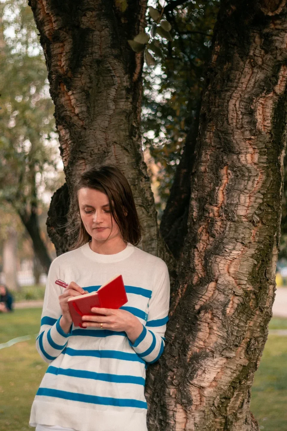 Georgia Blidar apoyada en el tronco de un árbol, escribiendo en una libreta roja