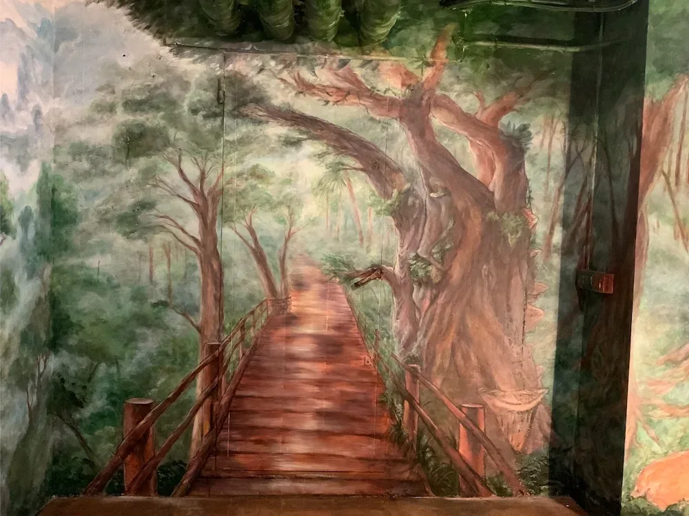Mural con ilusión óptica de bosque y pasarela de madera en restaurante