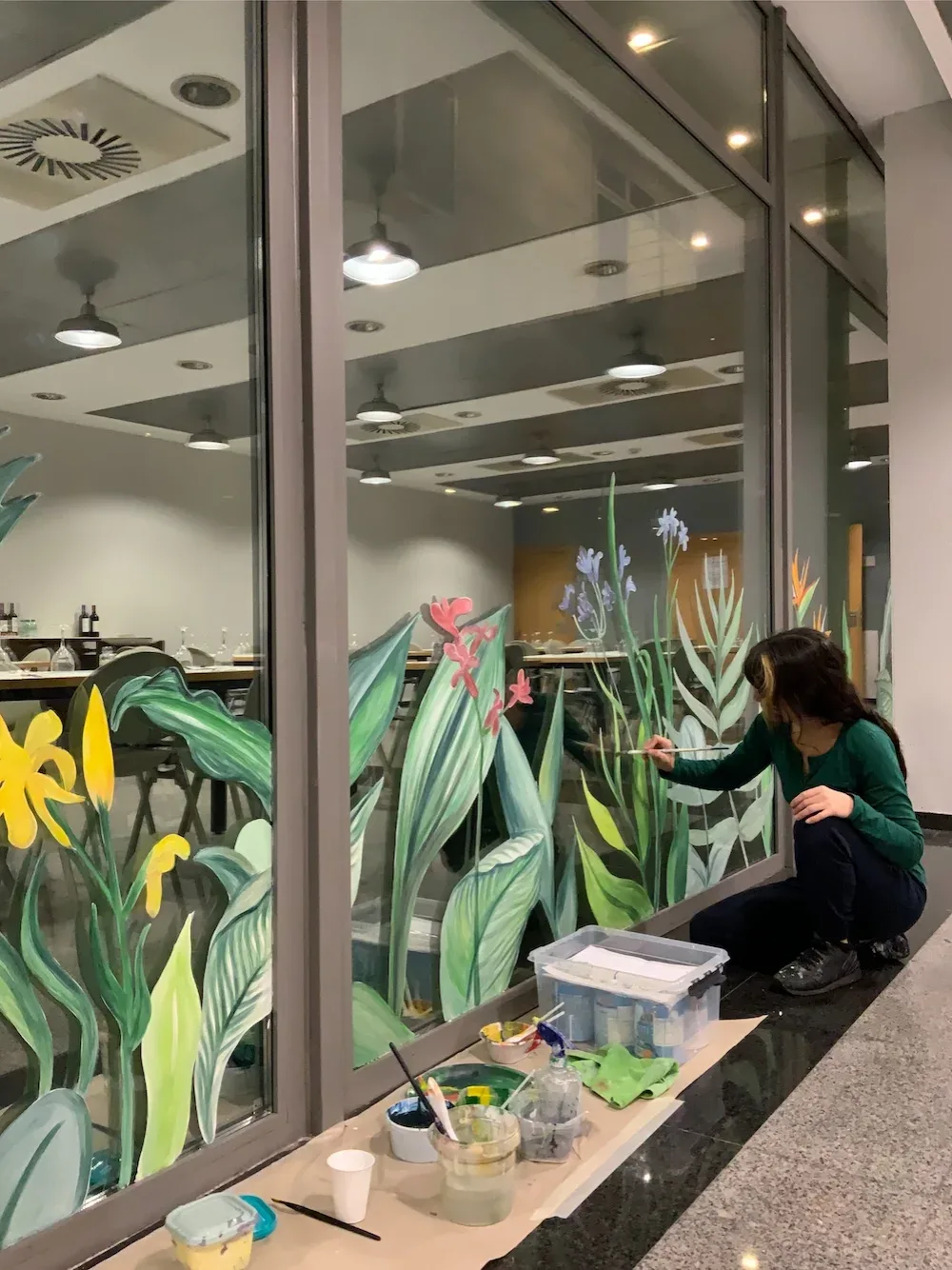 Diana pintando un mural botánico sobre cristal en restaurante